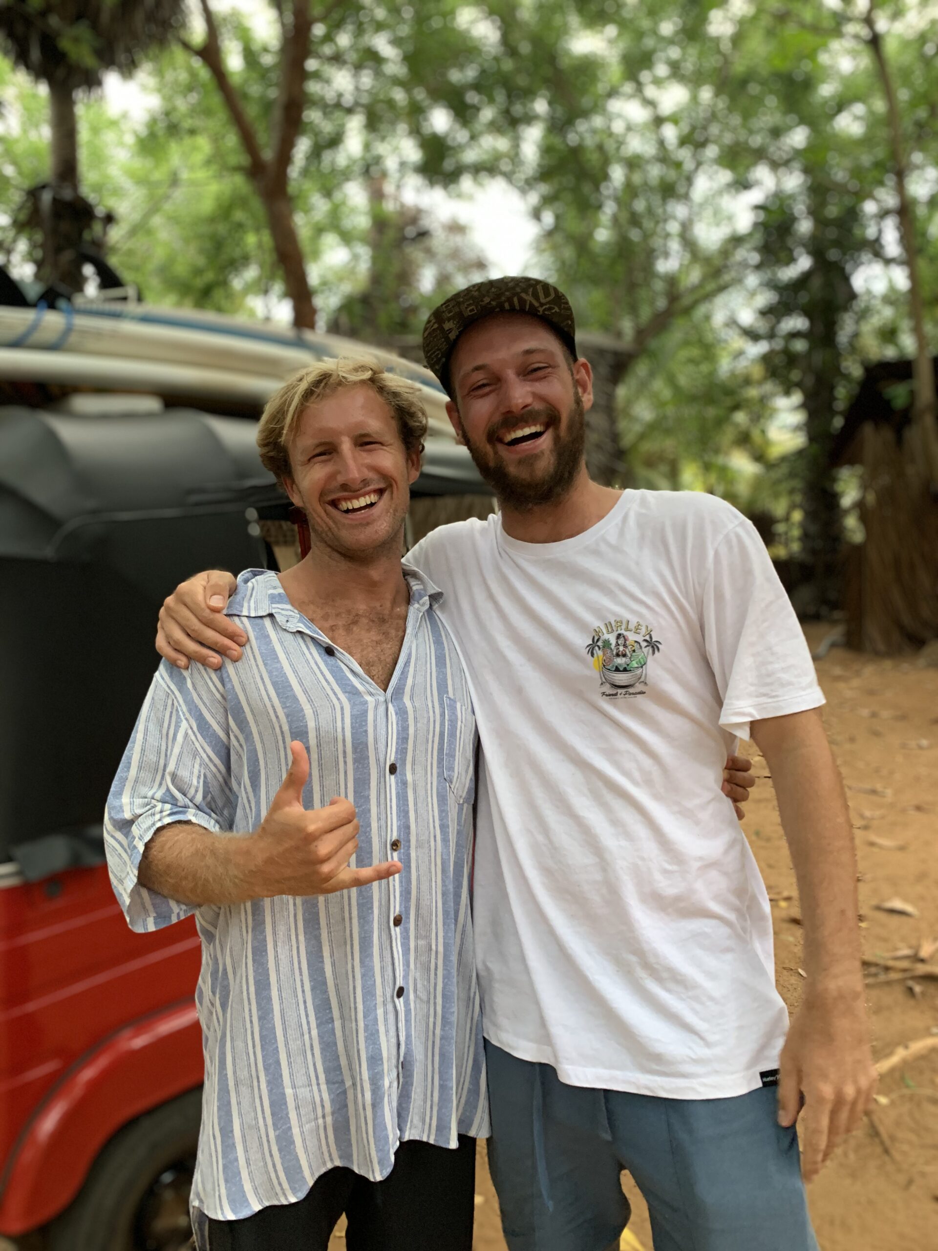 Surfing student of Surformer Wouter Byl happy with his surfing experience with a Tuk Tuk in the background with surfboards attached to the roof and tropical trees behind it.